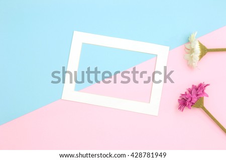 Empty frame and flowers flat lay on blue and pink pastel background with copy space. Soft effect filter.