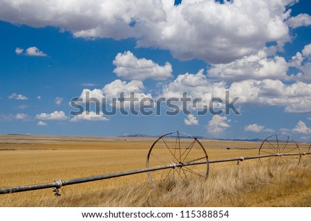 Photograph of an eye-catching agricultural field with irrigation equipment standing by along a country road in the great American west under the beauty of an awesome sky.