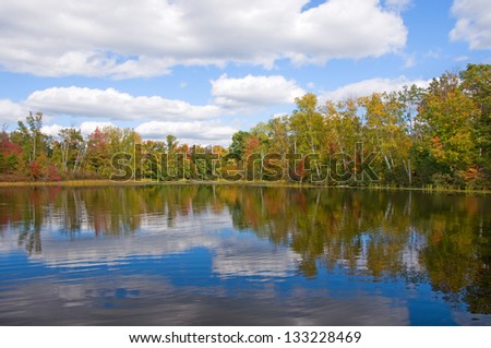 Photograph of a beautiful northwoods lake in early Autumn showing the beginning of changing colors, reflected in the water and accentuated by an amazing sky.
