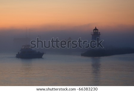 Photograph of a Lake Superior harbor entrance at dawn, before the sun is up, with a fishing boat heading out into the lake past a lighthouse.