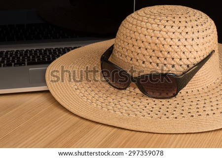 Sun hat and sunglasses with laptop on a desk