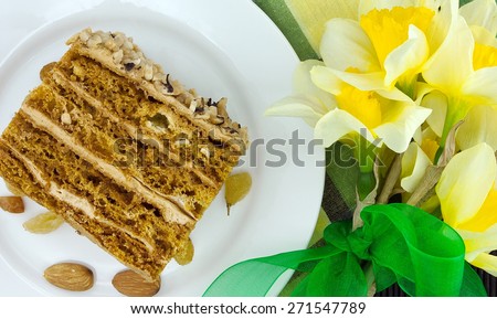 Cake slice with nut on plate. Bouquet of yellow daffodil or narcissus with green ribbon. Top view.