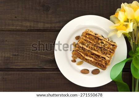 Cake slice with nut on plate on wooden table. Bouquet of yellow daffodil or narcissus with green ribbon. Top view