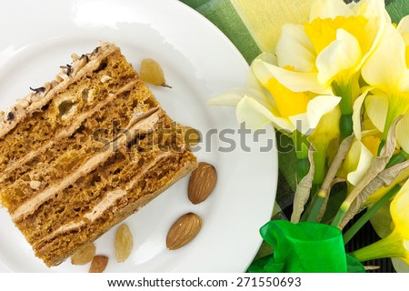 Cake slice with nut on plate. Bouquet of yellow daffodil or narcissus with green ribbon. Top view