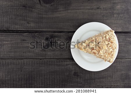 Layered cake slice with nut on plate, on wooden table, dark background. Top view.