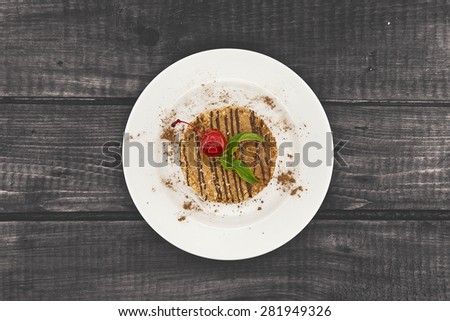 Layered cake with nut and cinnamon on plate, on wooden table, dark background. Top view.