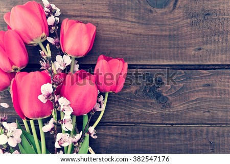Bouquet of red tulips and branches of sakura on a wooden background with copy space for greeting message. Spring flowers. Spring background. Top view