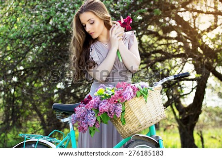 Beautiful girl in a long dress on a vintage bike with a bouquet of lilacs