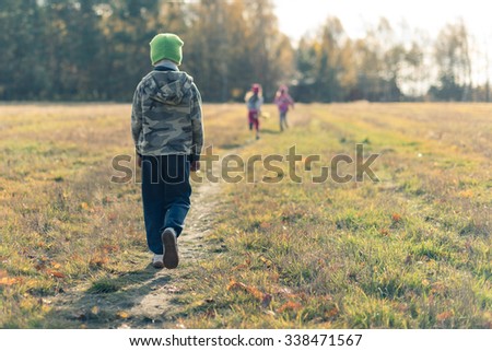 Sad boy walking behind laughing children