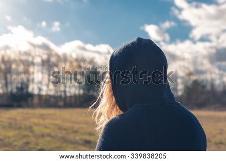 A shot from behind a young girl with blond long hair wearing a hood walking in a park