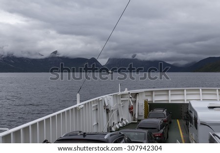 A ferry with cars and a cloudy landscape in the background