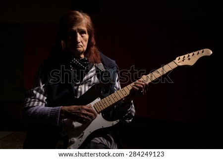 Funny elderly lady plays electric guitar in a dark room.
