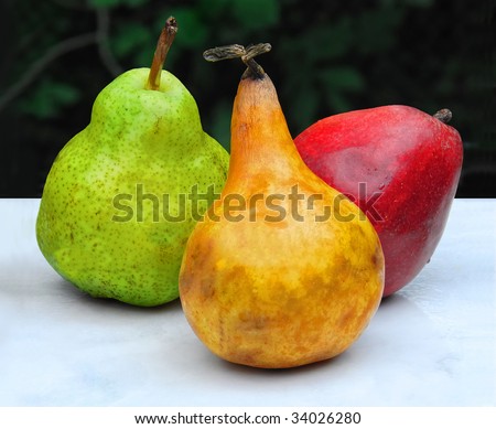 3 Pears: Artistic still life with three varieties of pear. Red yellow and green on a white surface against a dark background.