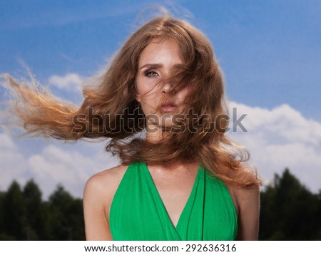 Beautiful blond girl in green dress on the field in summer forest.beauty young woman.Wind flying hair