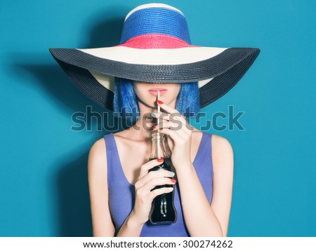 Beautiful young Woman in Hat drink soda. Fashion portrait. Elegance Beauty Girl with blue hair. colorful hat