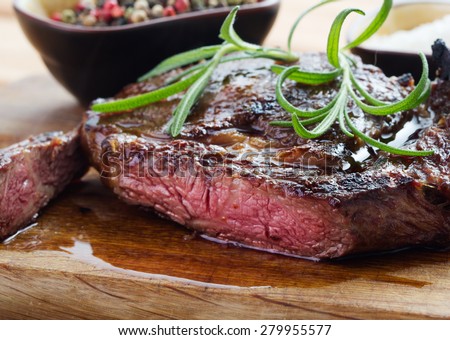 medium roast rib-eye steak on wooden plate with pepper and rosemary