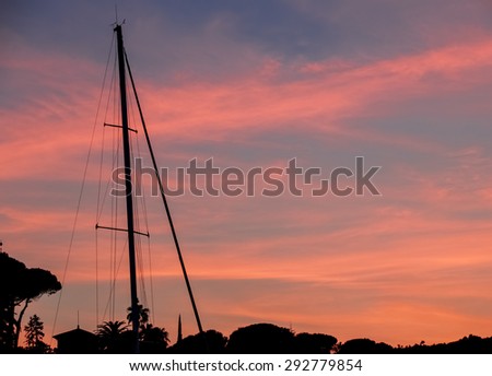 Silhouette of an one-masted touring boat in a harbor at sunset.