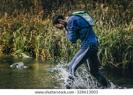 male athlete running across river. Rinses face with water