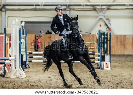 Chelyabinsk, Russia - November 22, 2015: male rider on horse galloping across field sports complex during Competitions Horse Show jumping
