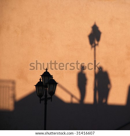 Warm evening light forms silhouette of three people and an antique style street lantern on the terracotta wall