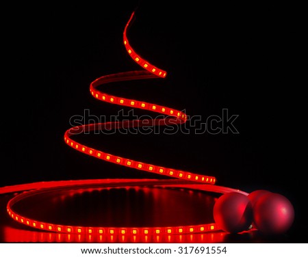 Red led stripe as Christmas tree with Christmas decorations on the black background