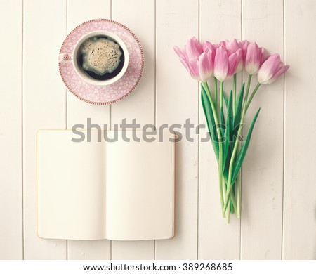 Pink tulips, coffee cup and notebook over white wood table ina flat lay composition