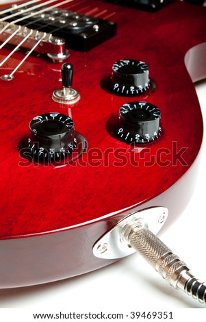 Detail of a wine red color electric guitar with cord plugged into the jack.