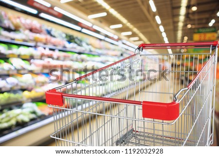 supermarket grocery store with fruit and vegetable shelves interior defocused background with empty red shopping cart
