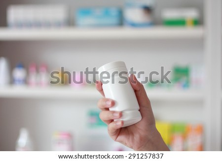 Blank white medicine bottle in pharmacist hand with blur shelves of drug in the pharmacy drugstore background