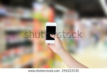 Female hand holding mobile smart phone on Supermarket blur background, business concept