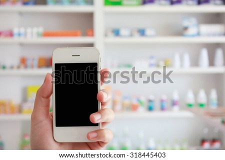 closeup pharmacist hand holding smart phone with blur some shelves of drug in the pharmacy drugstore
