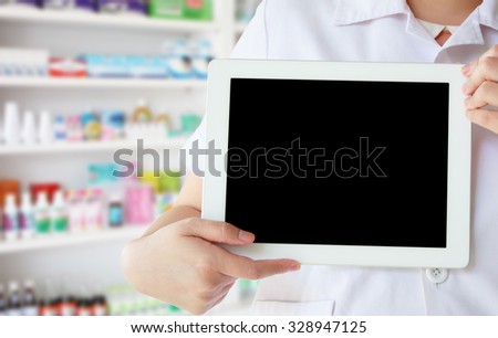 pharmacist in white coat showing blank digital tablet computer with shelves of drugs in the pharmacy store