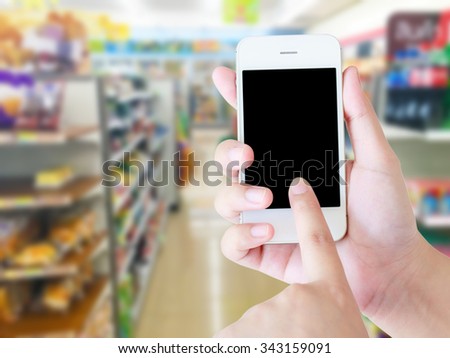 Hand holding mobile with blur supermarket shelves background, Online shopping concept.