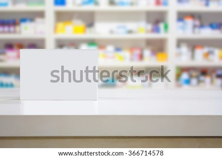 Blank white medicine package on counter with blur shelves of drug in the pharmacy drugstore