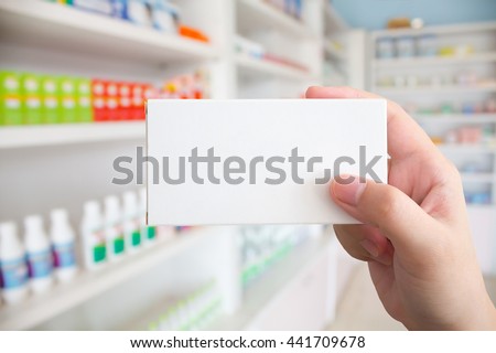 Close up pharmacist hand hold medicine box package with shelves of drugs in the pharmacy