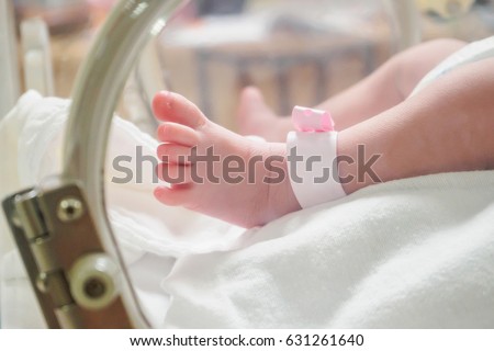 Newborn girl baby inside incubator in hospital post delivery room with identification bracelet tag name