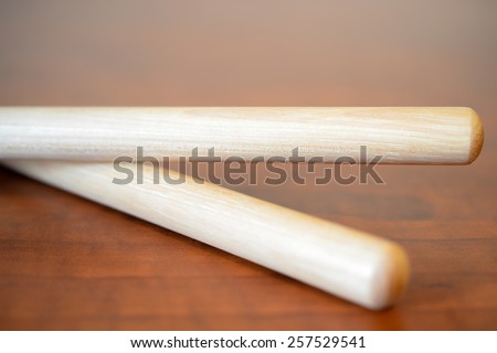 A pair of plain wooden drumsticks crossed on a faux wood surface with room for text