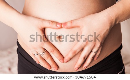 Pregnant Woman holding her hands in a heart shape on her baby bump. Pregnant Belly with fingers Heart symbol. Maternity concept. Baby Shower