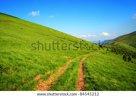 dirt long road among green hills and blue sky