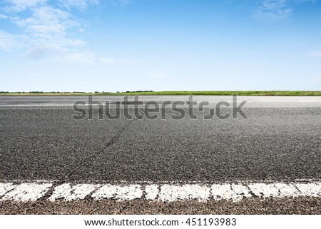 Asphalt road closeup with blue sky on horizon. Selective focus on foreground