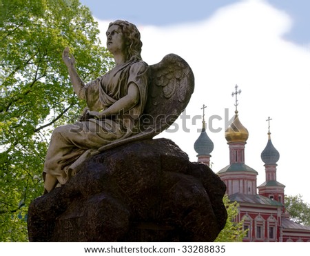 antique statue of angel on big black stone and church in backdrop at Novodevichiy Monastery in Russia, Moscow