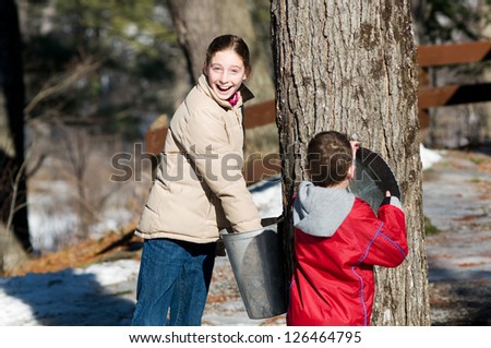 two children looking in a sap bucket at a sugar bush