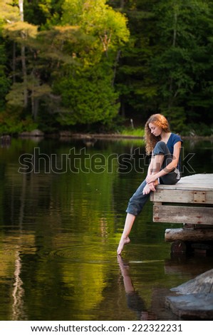 pretty teen girl on a lakeside dock in summer dipping her toe in the water