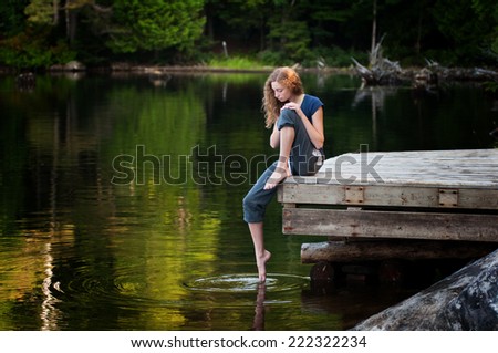 pretty teen girl on a lakeside dock in summer with her foot in the water