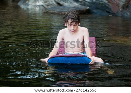 young boy playing in a lake with a boogie board