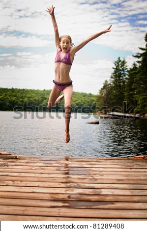 happy girl jumping off a dock into a lake