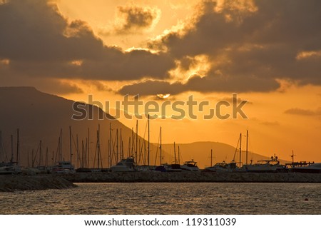 Sunset over marina. Postcard-like landscape: the sea, the hills, the clouds and golden sun setting. Horizontal shot.