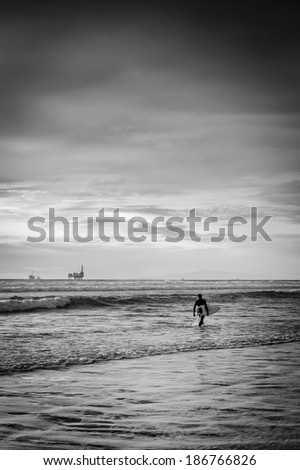 A black and white shot of a surfer walking on the beach looking for a good set of waves.
