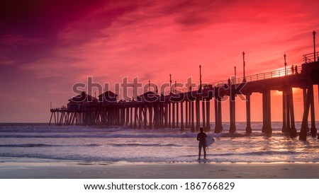 A wide shot of a surfer  looking for a good set of waves and the Huntington Beach Pier in the background.