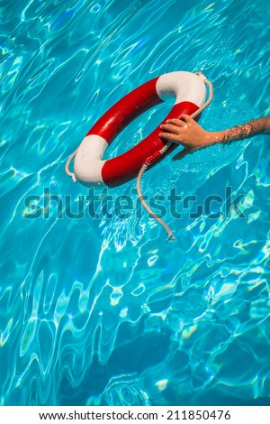A close up shot of a life guards red and white rescue ring buoy floating in a pool with a child\'s hand reaching for the buoy.